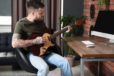 Photo of Handsome hipster man playing guitar in stylish room