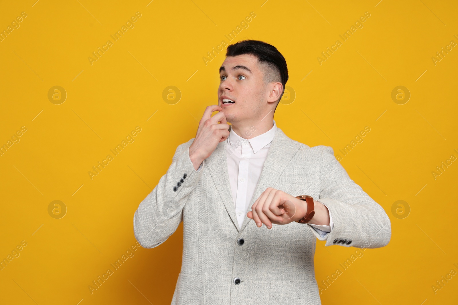 Photo of Emotional young man checking time on orange background. Being late concept