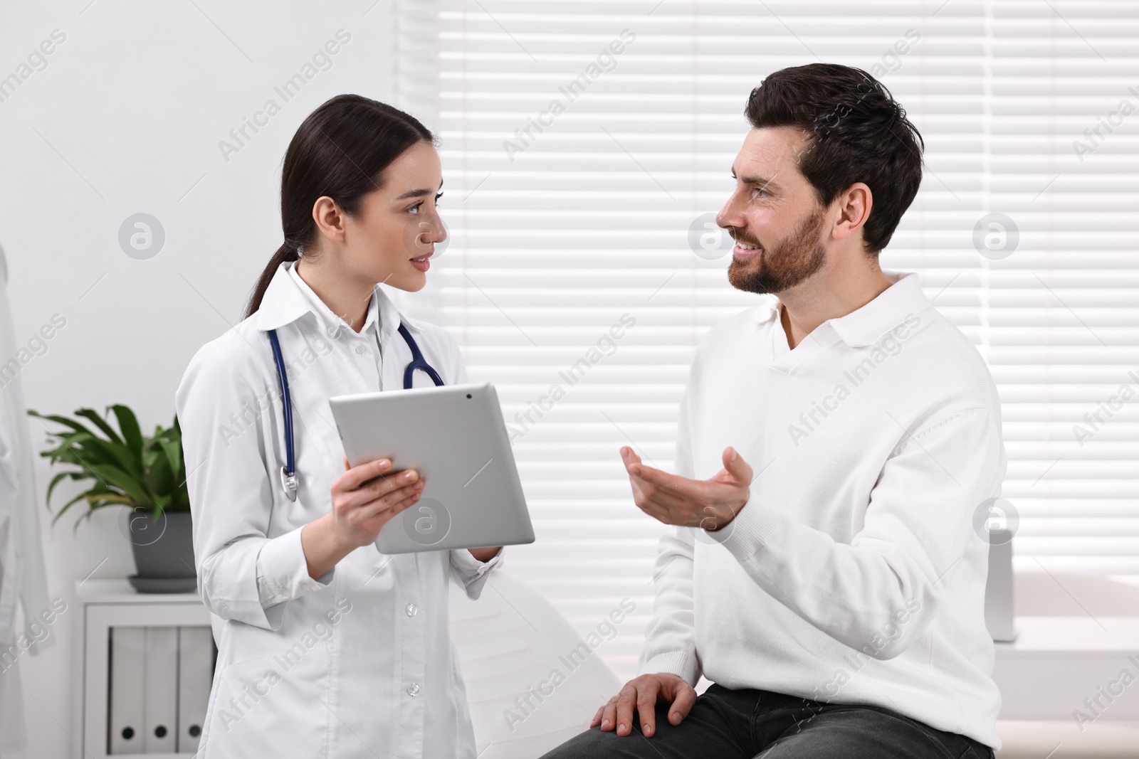 Photo of Doctor with tablet consulting patient during appointment in clinic