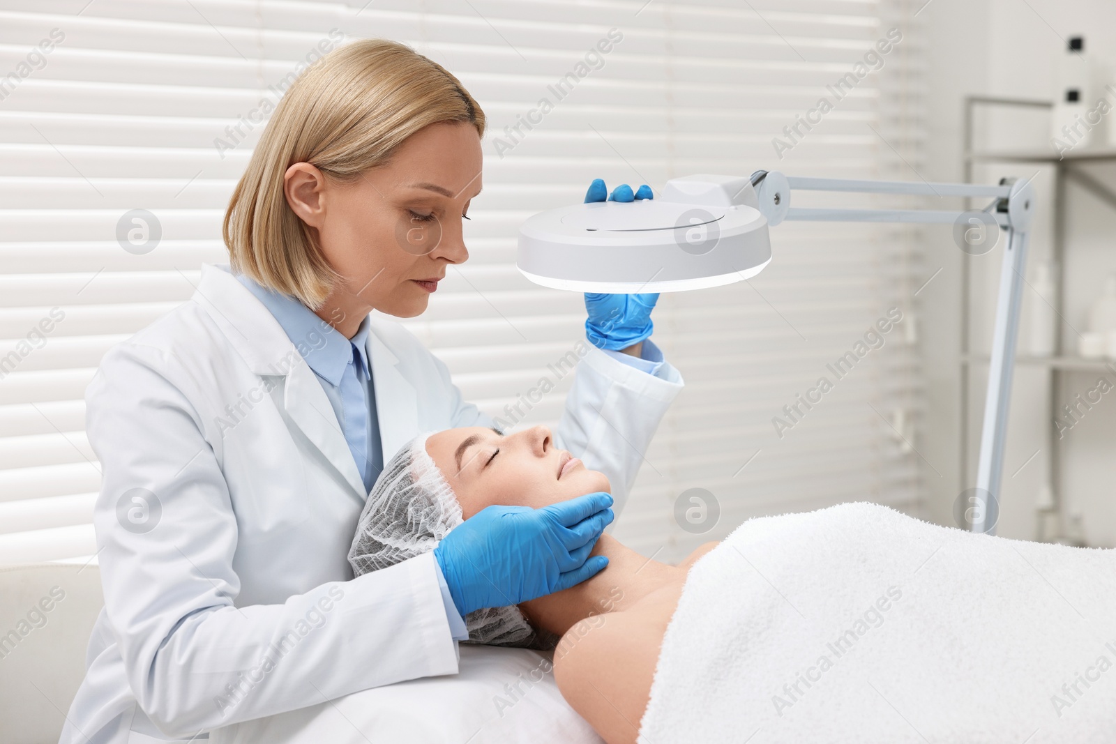 Photo of Dermatologist examining patient`s face under lamp in clinic