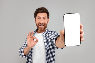 Photo of Handsome man showing smartphone in hand and OK gesture on light grey background, selective focus. Mockup for design