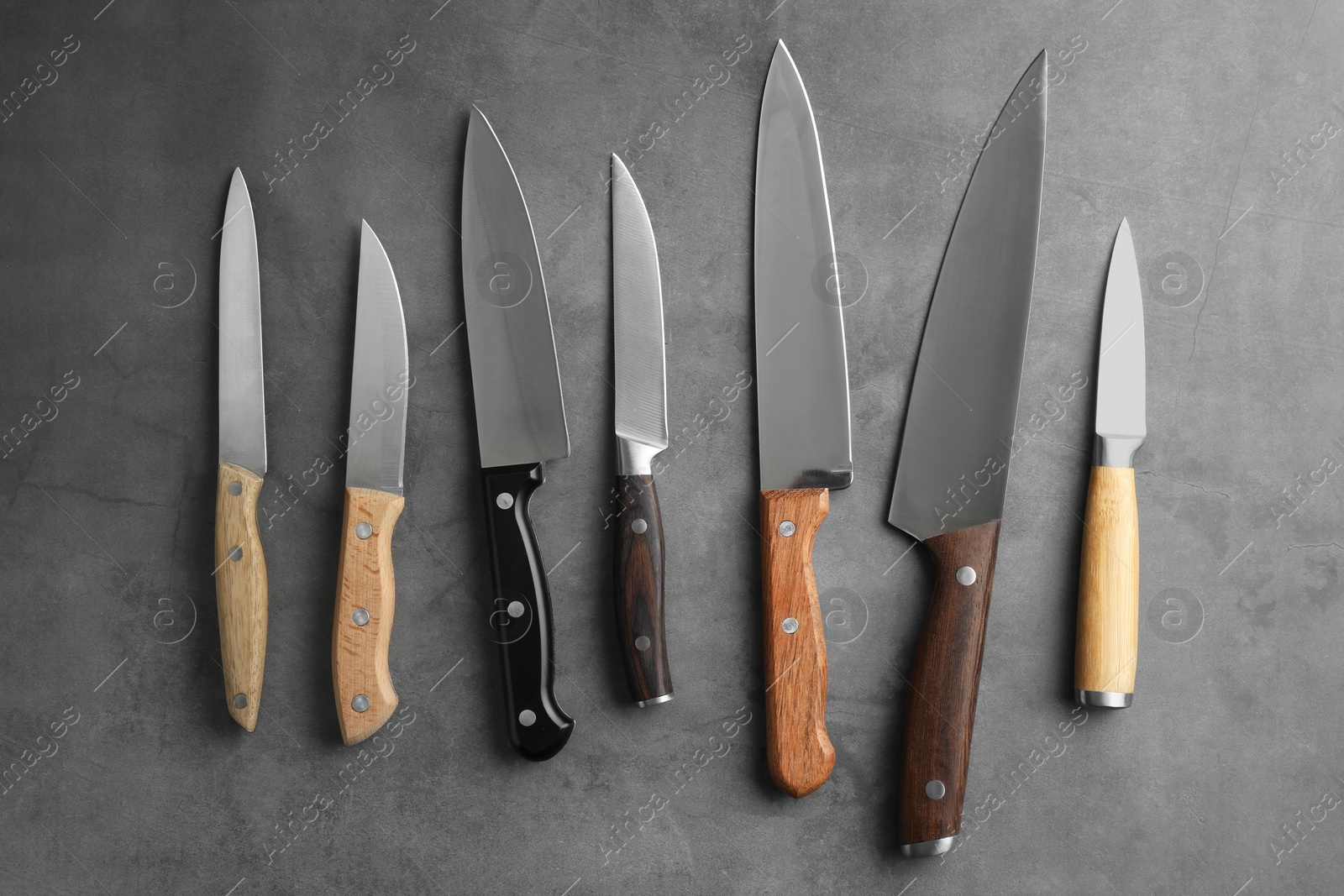 Photo of Many different knives on grey textured table, flat lay