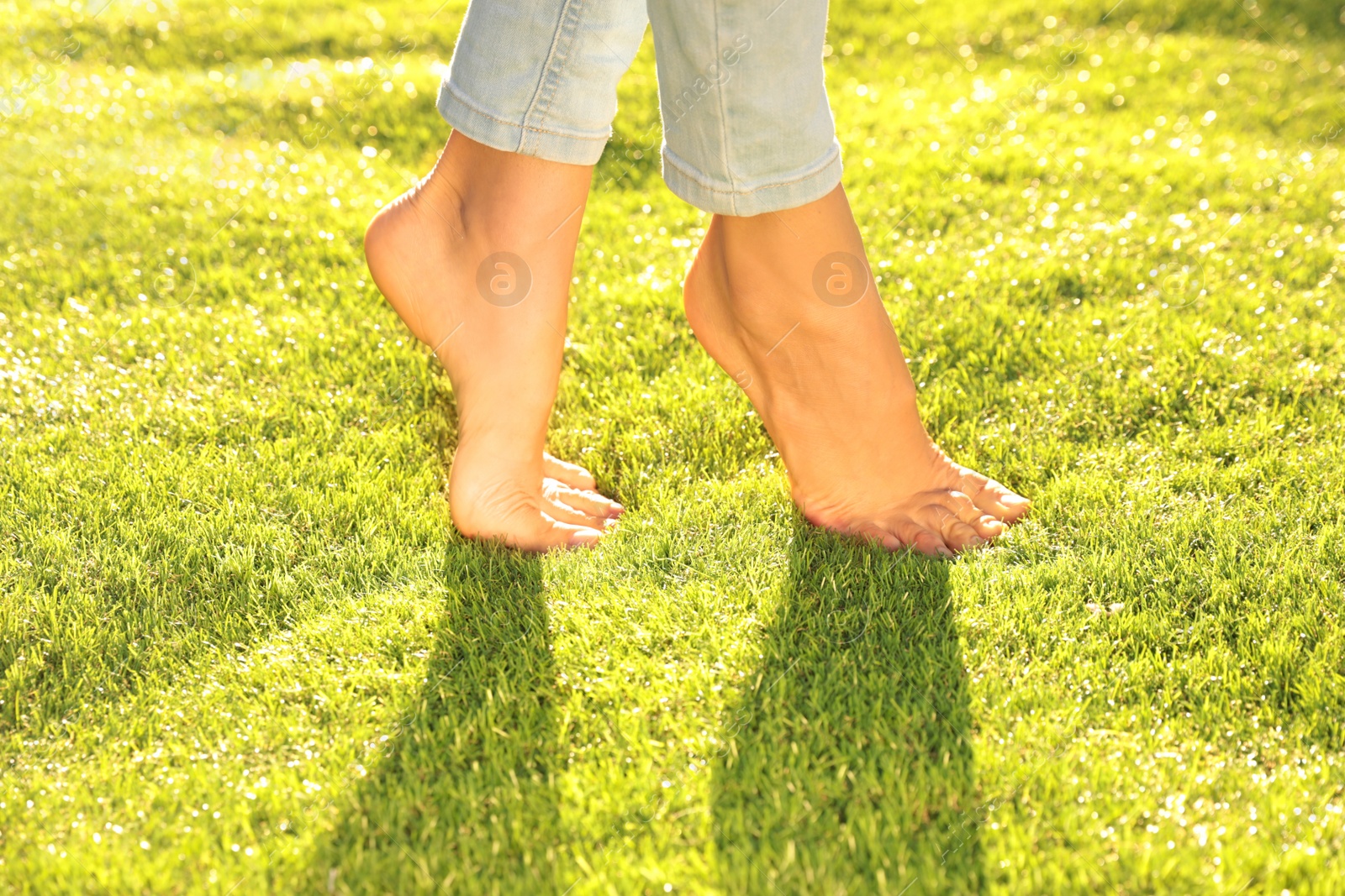 Photo of Young woman walking barefoot on fresh green grass, closeup