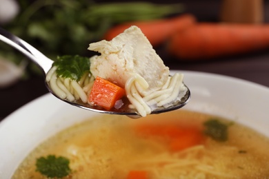 Spoon with fresh homemade chicken soup on blurred background, closeup