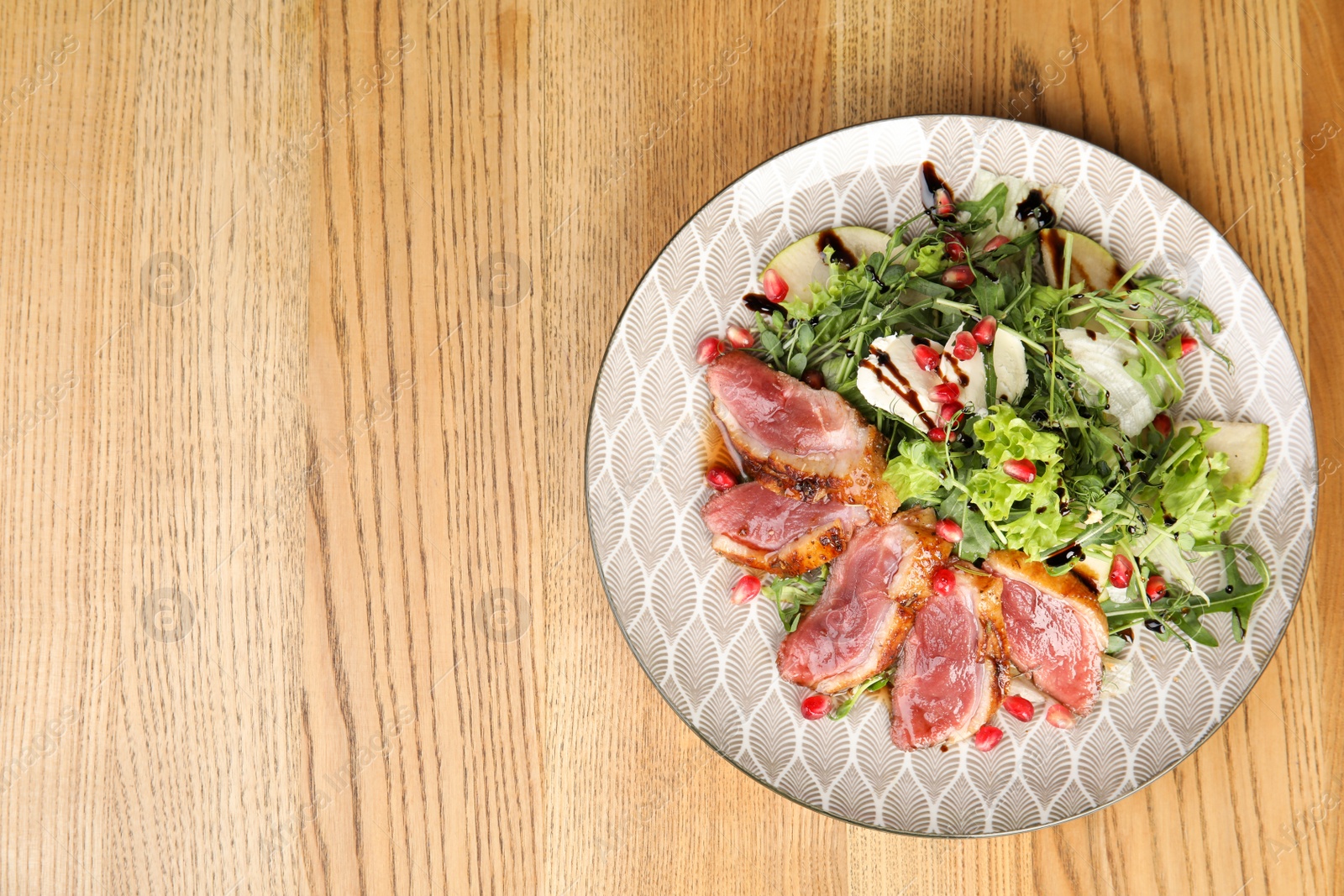 Photo of Delicious salad with roasted duck breast served on wooden table, top view. Space for text