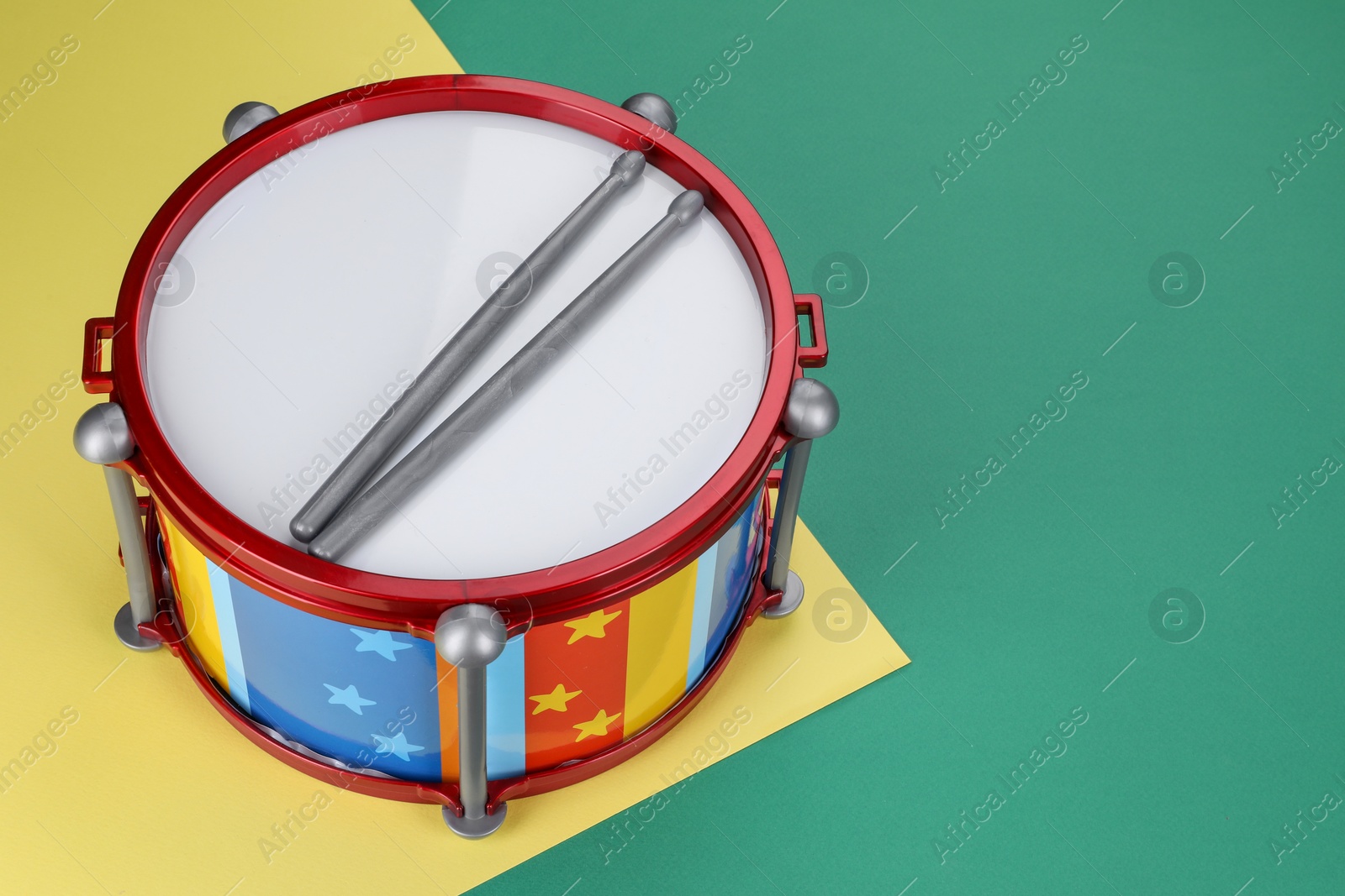 Photo of Children's drum with drumsticks on color background. Space for text