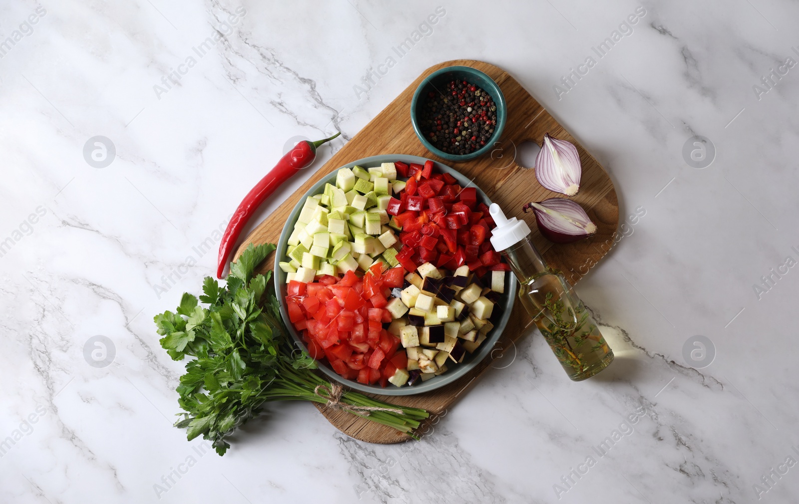 Photo of Cooking delicious ratatouille. Fresh ripe vegetables and plate on white marble table, flat lay