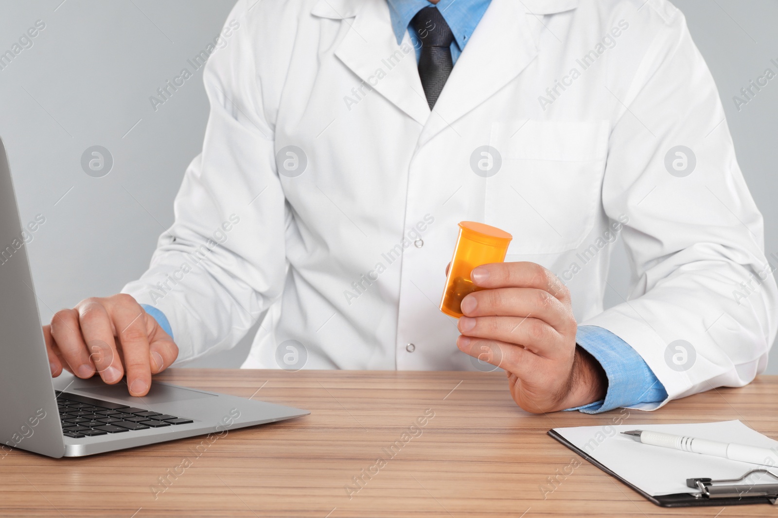 Photo of Professional pharmacist working with laptop at table against light grey background, closeup