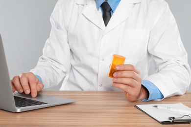 Photo of Professional pharmacist working with laptop at table against light grey background, closeup