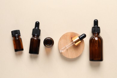 Bottles of cosmetic serum on beige background, flat lay