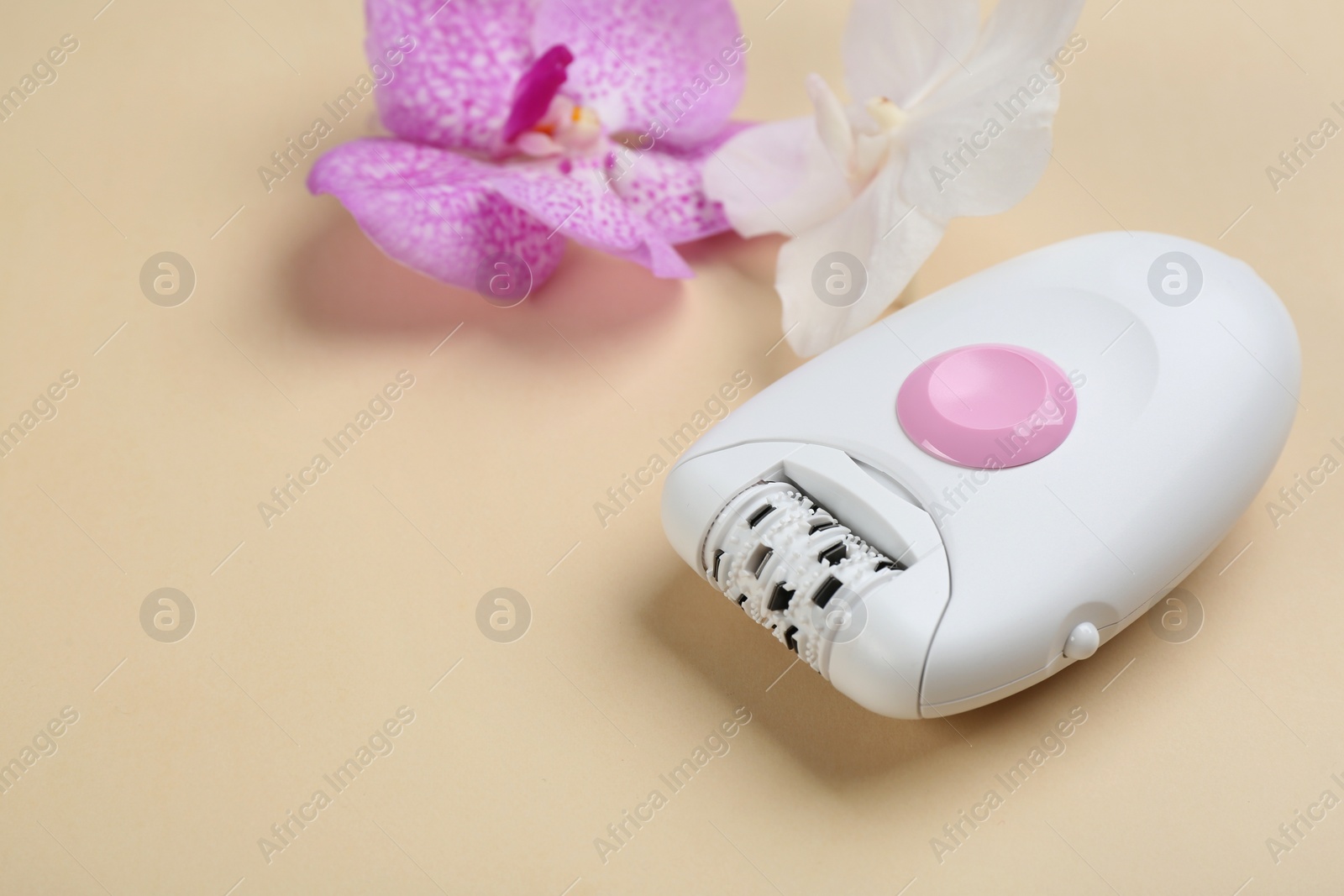 Image of Modern epilator and orchid flowers on beige background. Space for text