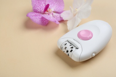 Modern epilator and orchid flowers on beige background. Space for text