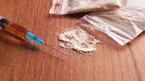 Plastic bags of powder and syringe on wooden table, closeup. Hard drugs