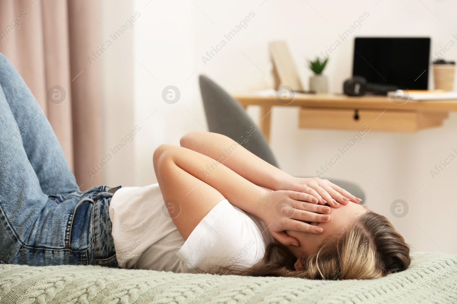 Photo of Unhappy teenage girl covering face with hands on bed at home