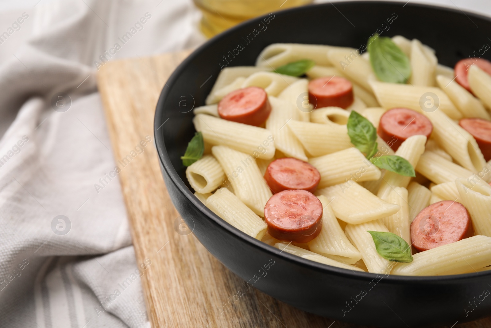 Photo of Tasty pasta with smoked sausage and basil in bowl on table, closeup