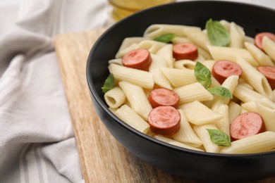 Tasty pasta with smoked sausage and basil in bowl on table, closeup