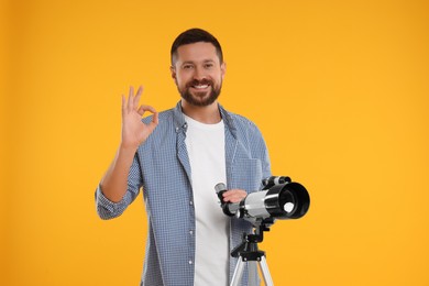 Happy astronomer with telescope showing ok gesture on orange background