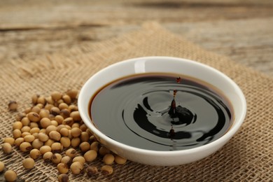 Photo of Soy sauce in bowl and beans on wooden table, closeup