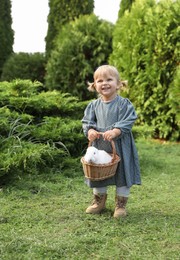 Photo of Happy little girl holding wicker basket with cute rabbit outdoors on sunny day