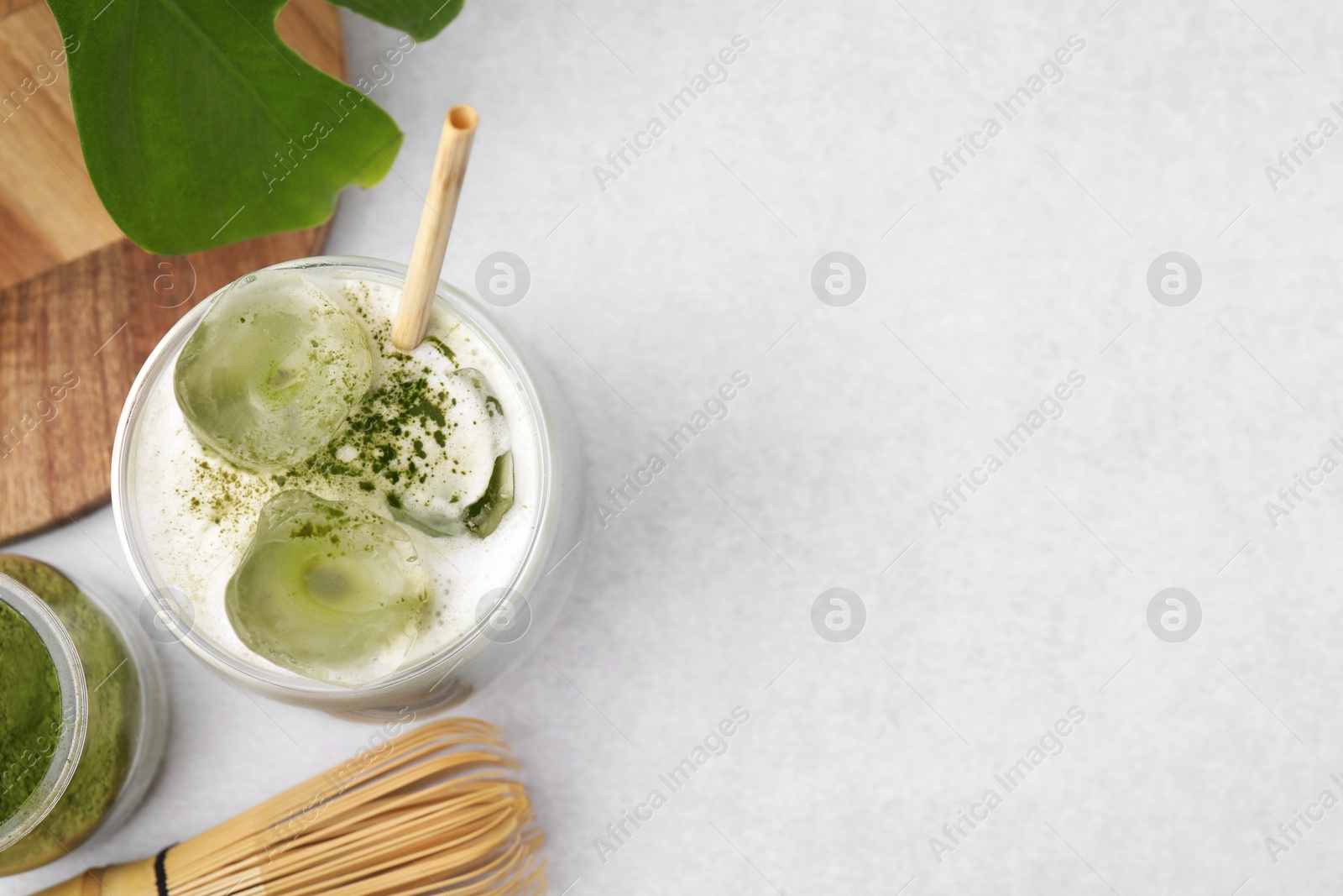 Photo of Glass of tasty iced matcha latte, leaf, powder and bamboo whisk on white table. Space for text