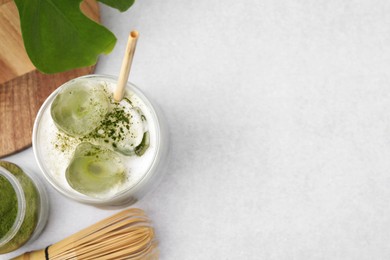 Glass of tasty iced matcha latte, leaf, powder and bamboo whisk on white table. Space for text