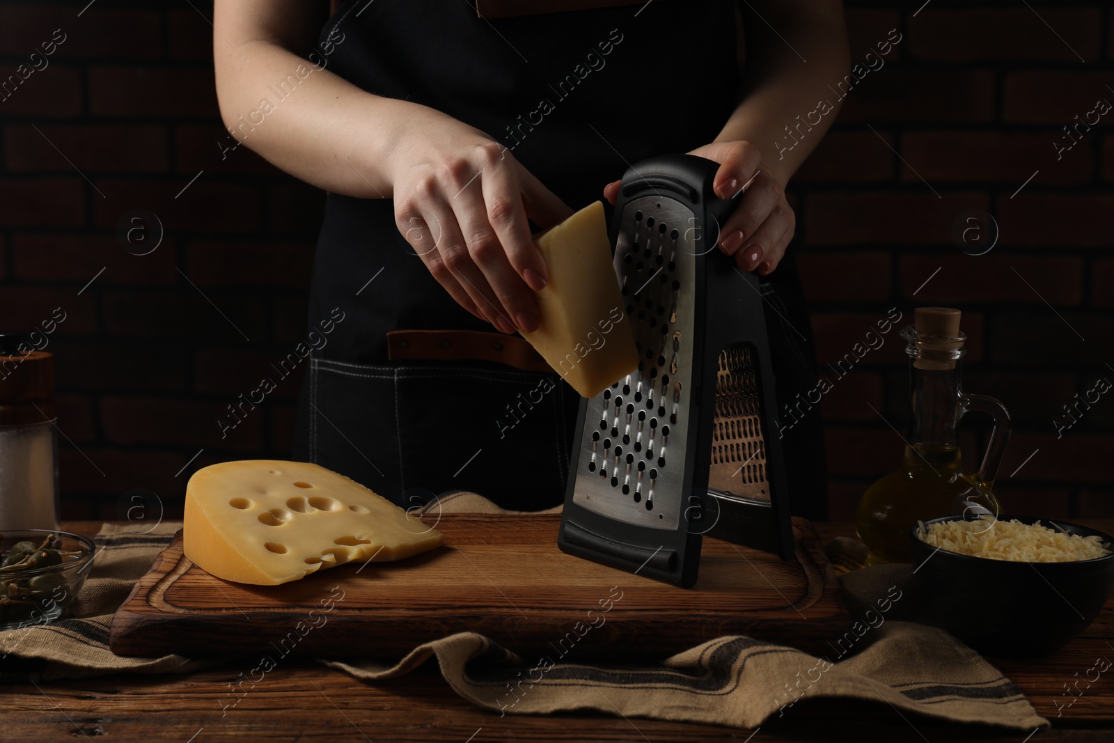 Photo of Woman grating cheese at wooden table, closeup