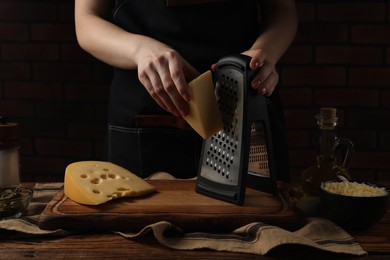 Woman grating cheese at wooden table, closeup