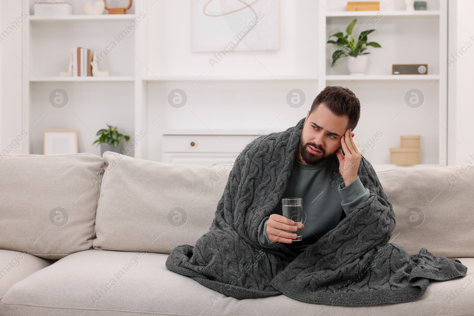 Photo of Man with glass of water suffering from headache on sofa at home. Space for text