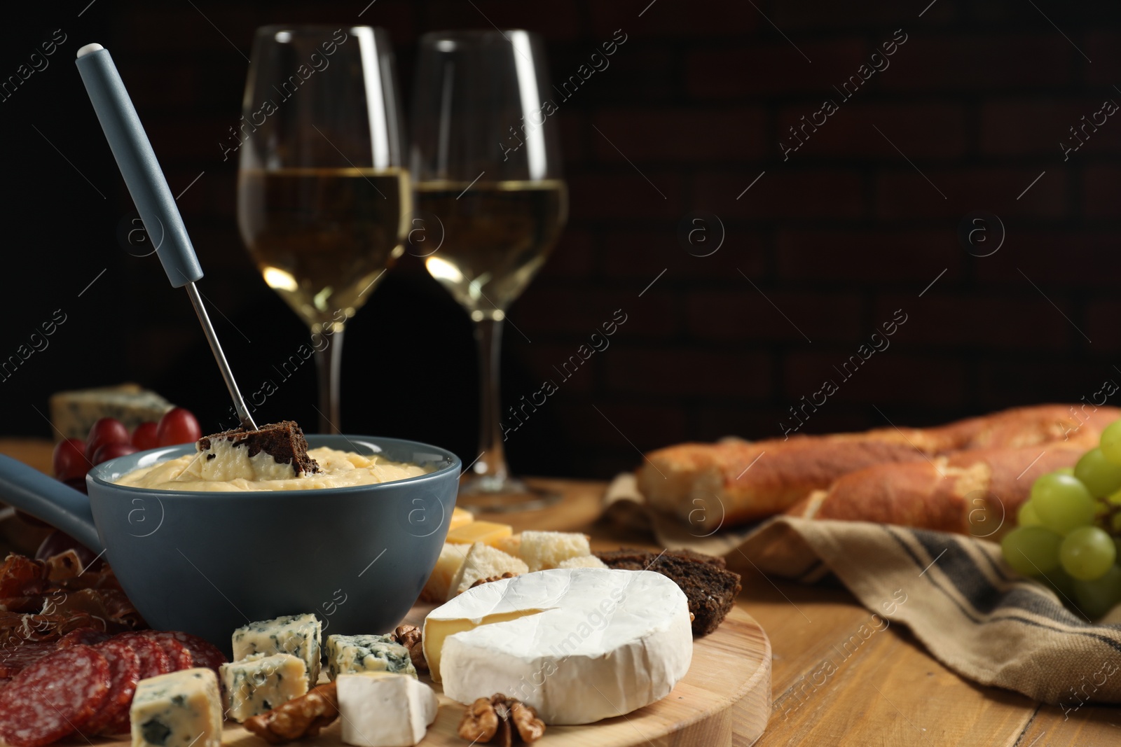 Photo of Fondue pot with tasty melted cheese, fork, different snacks and wine on wooden table