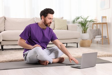 Man meditating near laptop at home, space for text