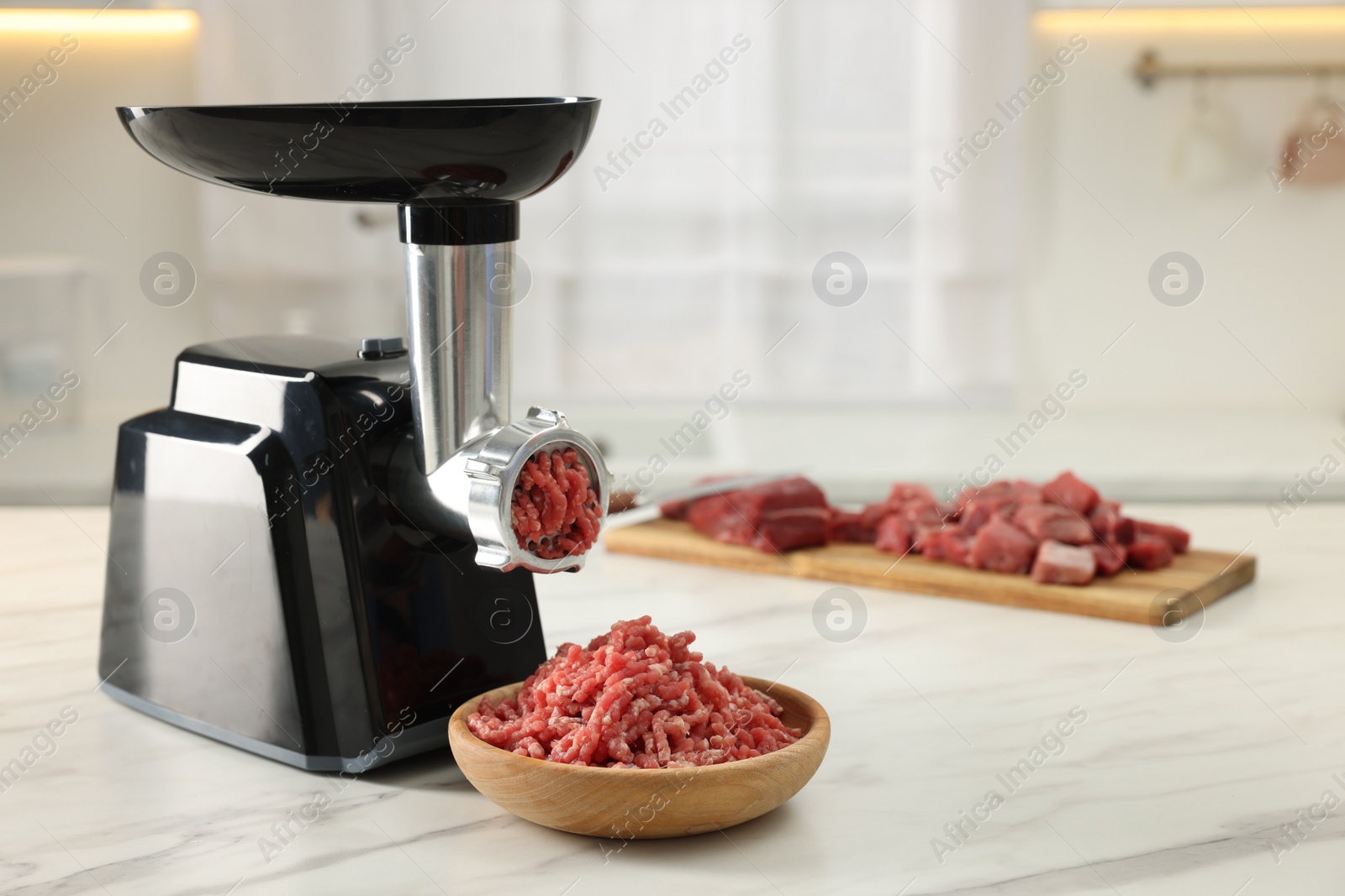 Photo of Electric meat grinder with minced beef on white marble table in kitchen, space for text