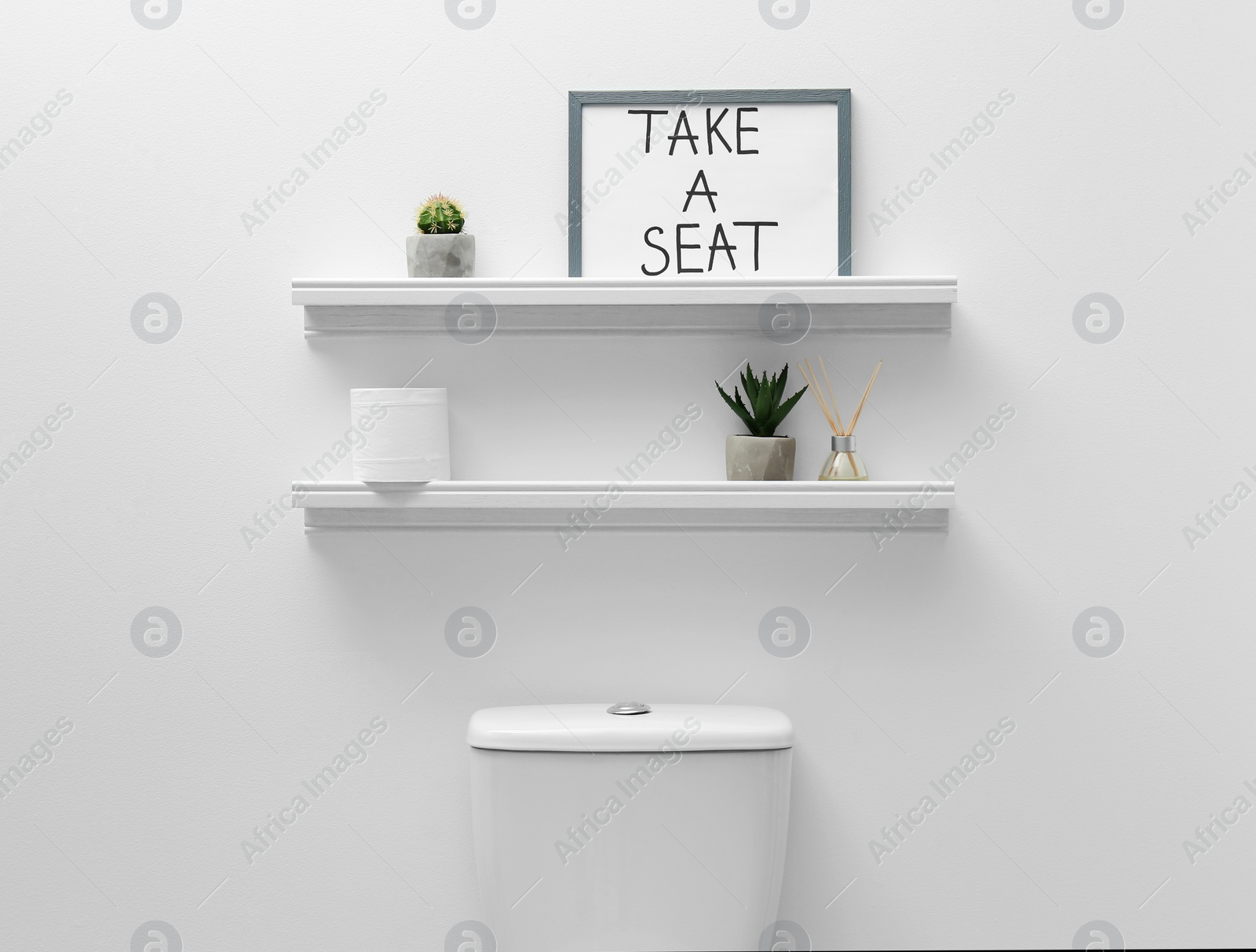 Photo of Toilet bowl, decor elements and funny sign near white wall. Bathroom interior