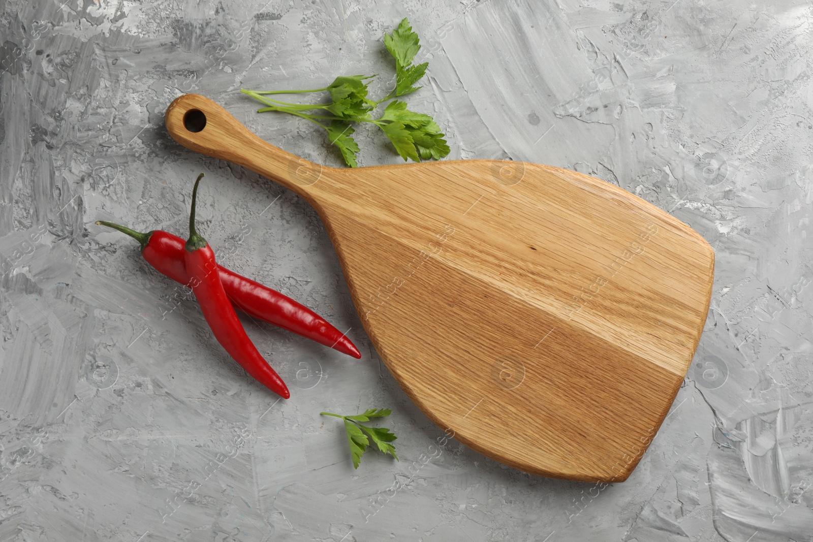 Photo of Cutting board, chili peppers and parsley on grey textured table, flat lay. Space for text