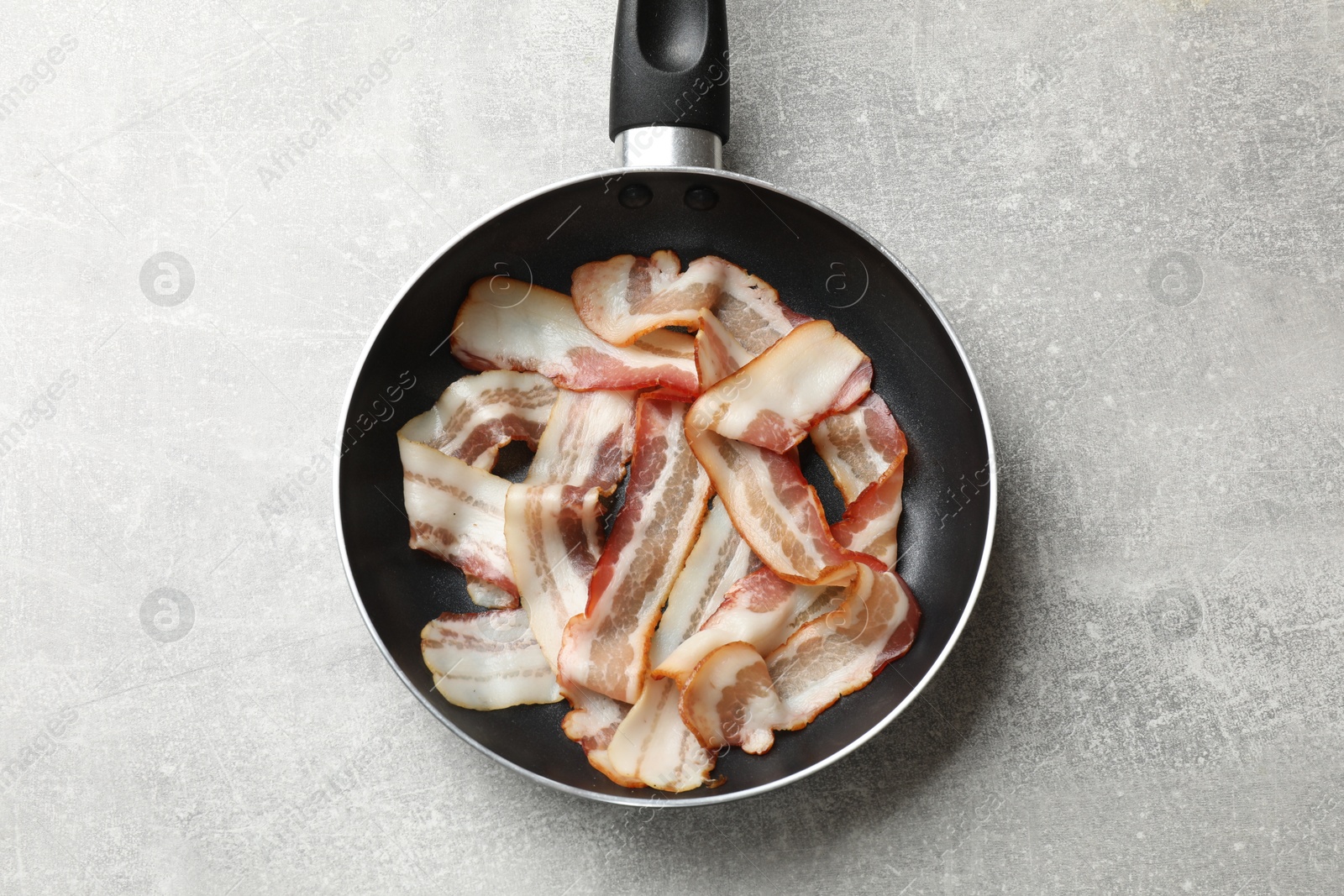 Photo of Delicious bacon slices in frying pan on light grey table, top view