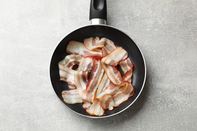 Photo of Delicious bacon slices in frying pan on light grey table, top view