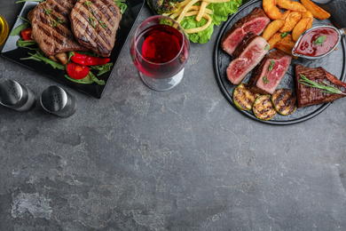 Delicious beef steaks and tenderloin served on grey table, flat lay. Space for text