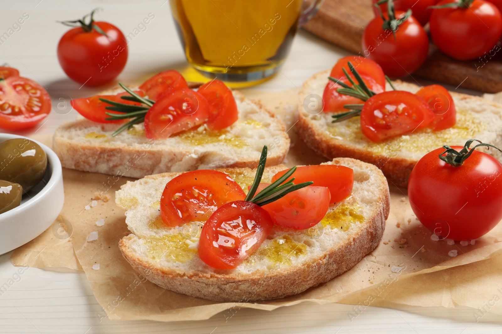 Photo of Tasty bruschettas with oil, tomatoes and rosemary on parchment paper, closeup