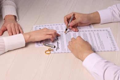 Man and woman signing marriage contract at light wooden table, closeup