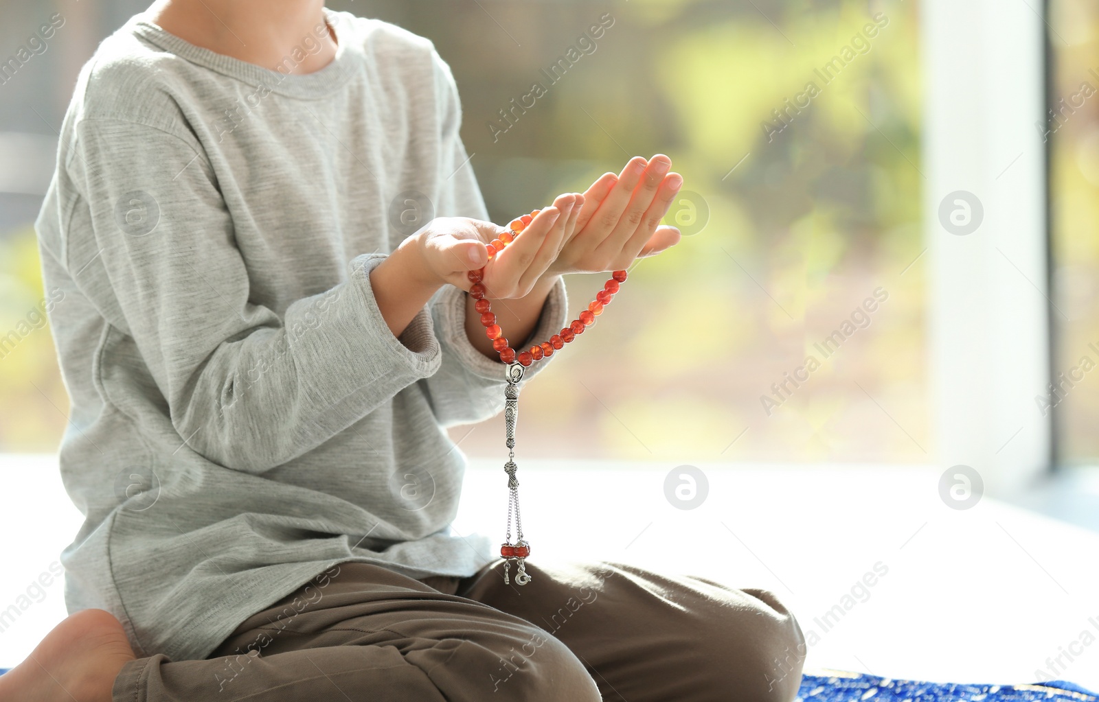 Photo of Little Muslim boy with misbaha praying indoors, closeup. Space for text