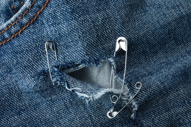 Photo of Hole in denim fabric fixed with metal safety pins, closeup