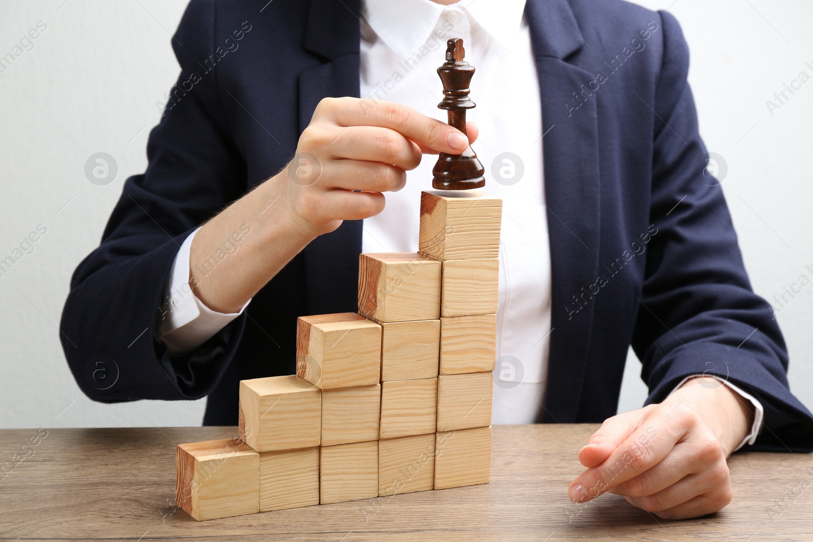 Photo of Woman putting chess piece on top of wooden stairs at table, closeup. Career promotion concept