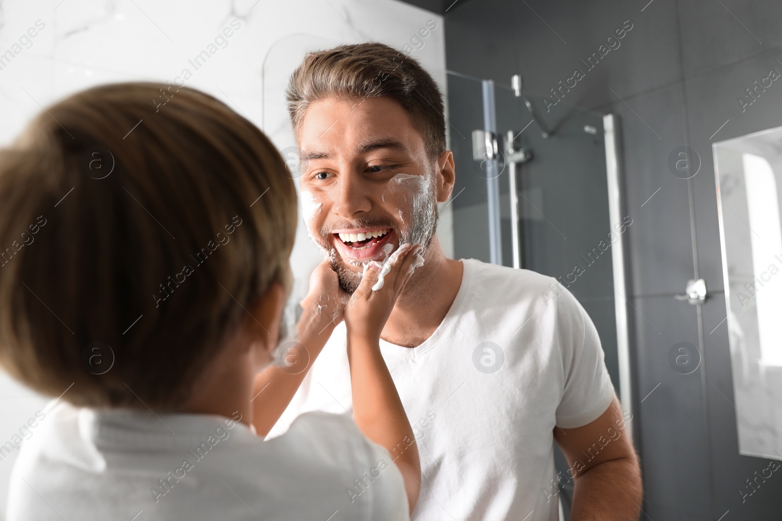 Photo of Dad and son with shaving foam on their faces having fun in bathroom