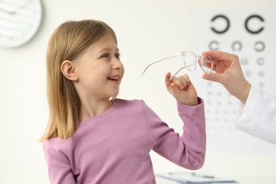 Vision testing. Ophthalmologist giving glasses to little girl indoors