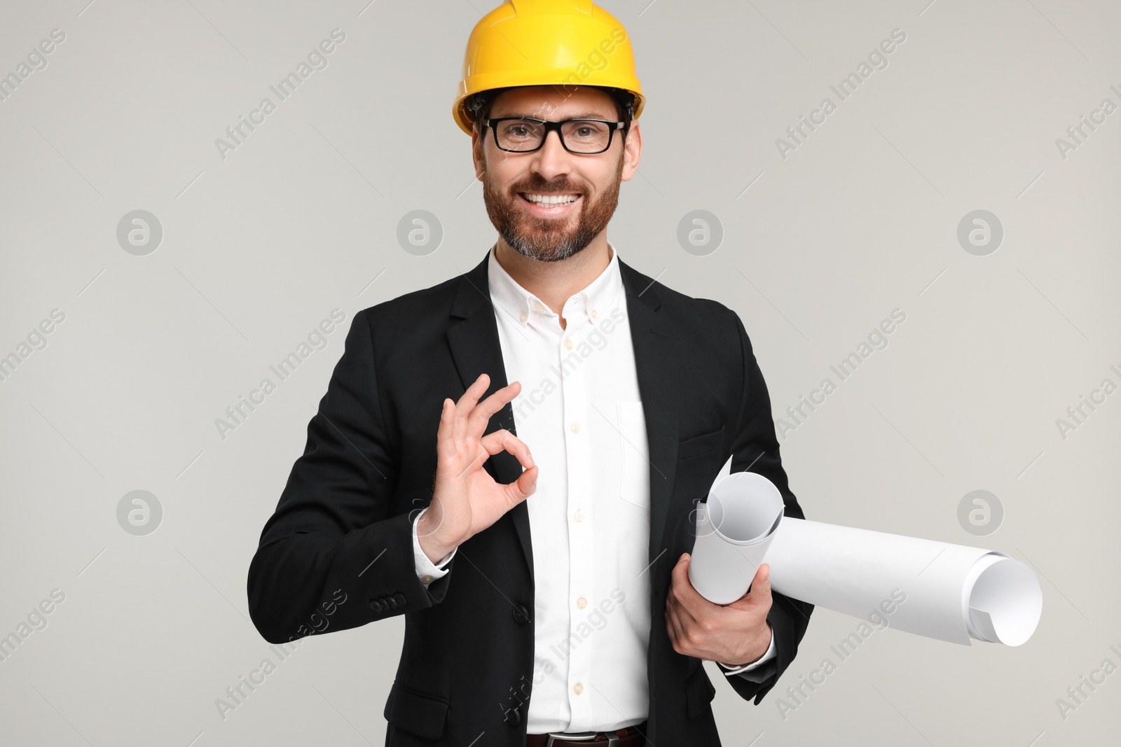 Photo of Architect in hard hat with drafts showing OK gesture on gray background