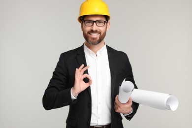 Architect in hard hat with drafts showing OK gesture on gray background