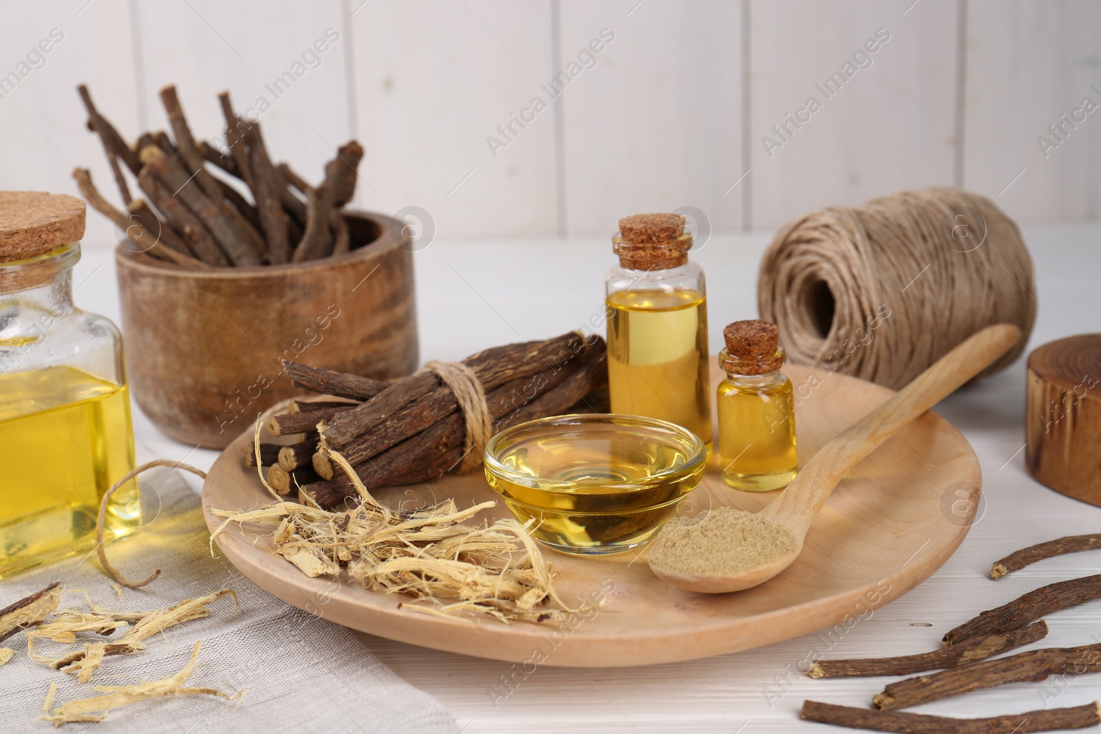 Photo of Dried sticks of licorice roots, powder and essential oil on white wooden table