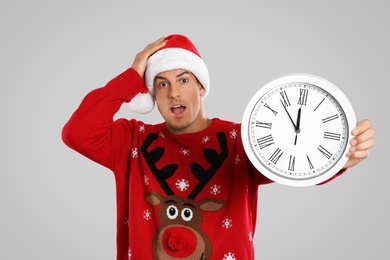 Man in Santa hat with clock on grey background. New Year countdown