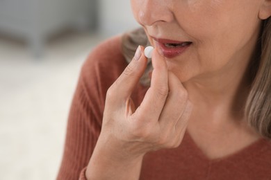 Photo of Senior woman taking pill on blurred background, closeup