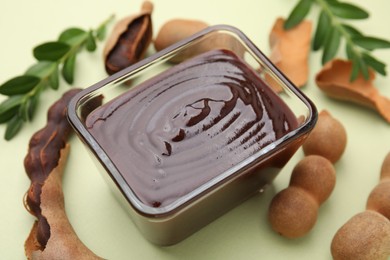 Photo of Bowl of tasty tamarind sauce and fresh pods on light green table, closeup