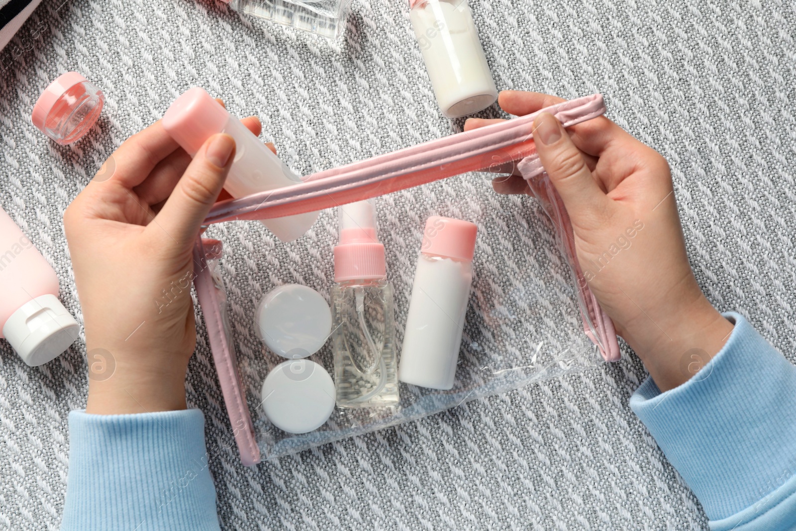 Photo of Cosmetic travel kit. Woman putting small bottle with personal care product into plastic bag on sofa, top view